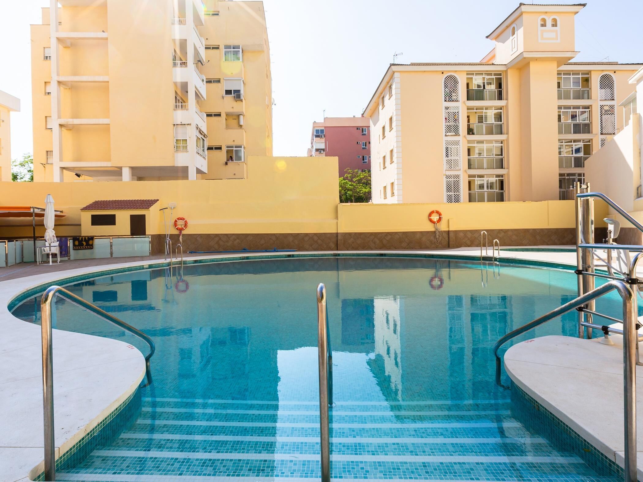 A swimming pool with a tiled deck, metal handrails, and a lifebuoy.