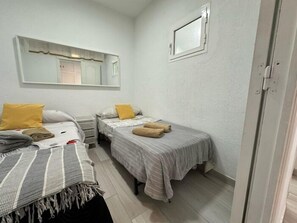 Een kleine, goed verlichte kamer met twee eenpersoonsbedden, een spiegel en een deur.