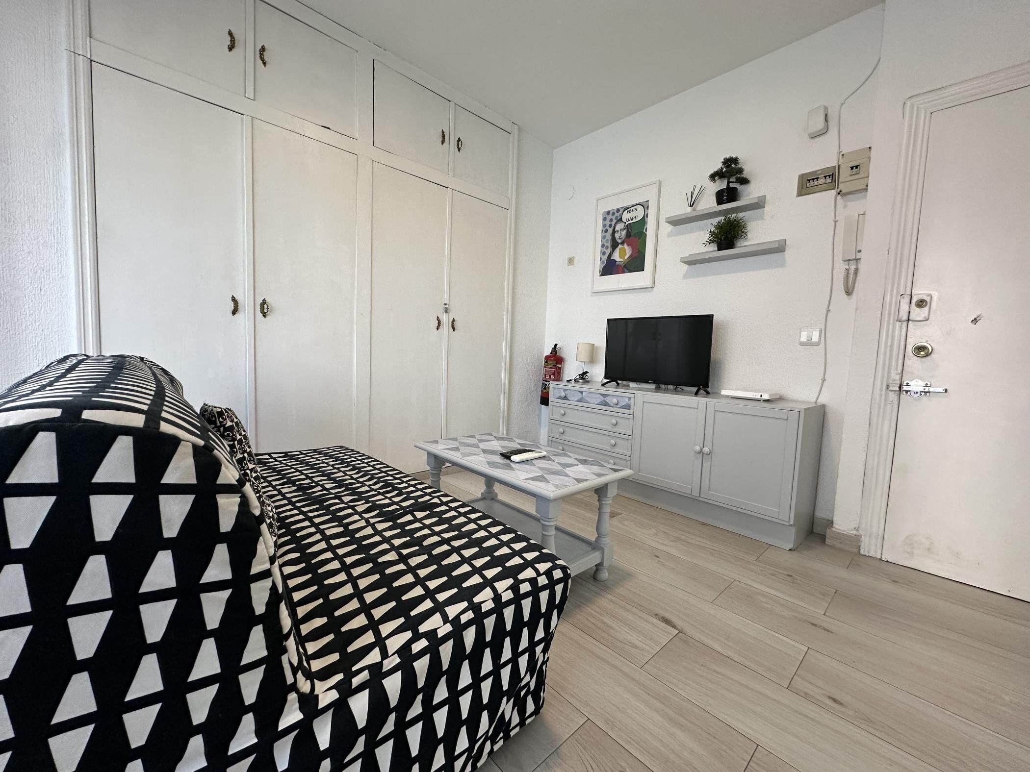 A living room with a patterned sofa, a TV on a cabinet, and a small table.