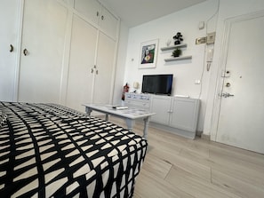 Quarto com cama, escrivaninha, televisão e guarda-roupa.