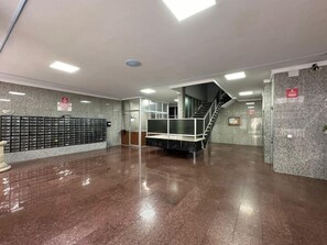 Een ruime lobby met een trap, een receptiebalie en een wand met lockers.