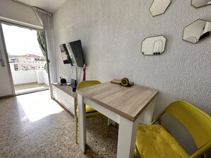 A room with a dining table, yellow chairs, a flat-screen TV mounted on the wall, and a view of buildings outside. - Studio with Sea-View Terrace, Pool and WiFi in Central Torremolinos (Torremolinos)