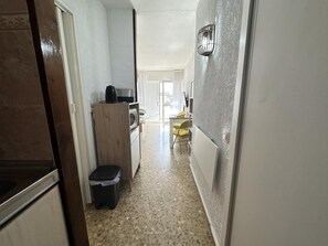 A narrow hallway with a kitchen area on the left, a trash bin, and a small table with a chair on the right. - Studio with Sea-View Terrace, Pool and WiFi in Central Torremolinos (Torremolinos)