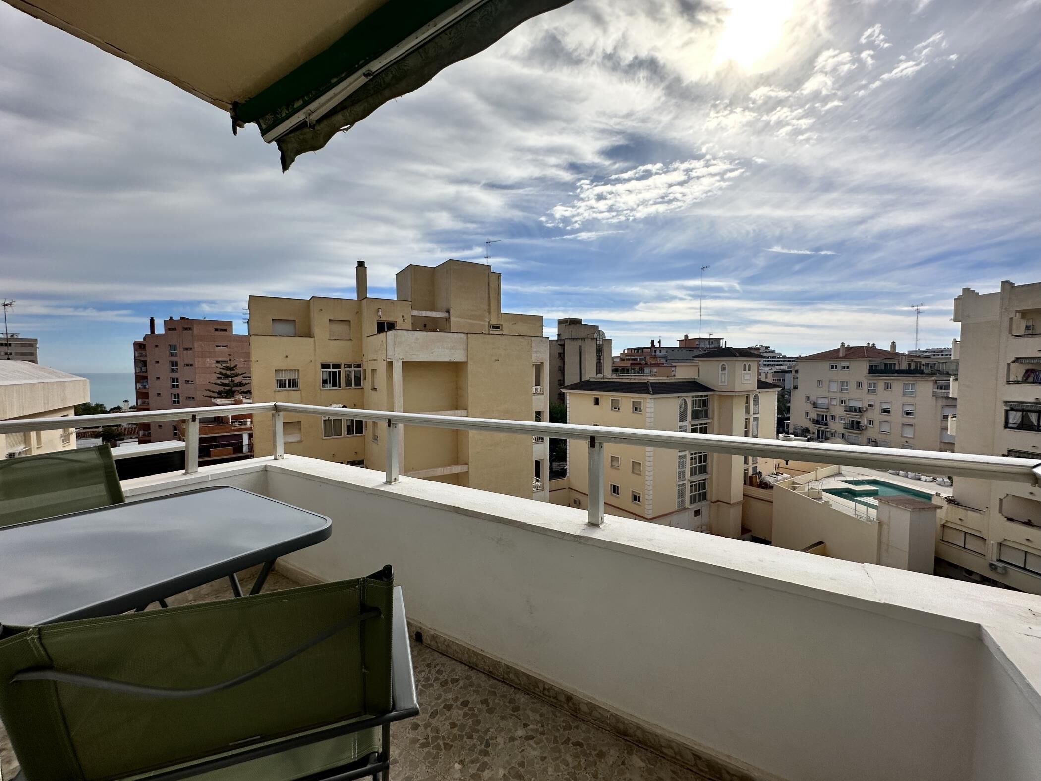 A balcony with a table and chairs, overlooking a cityscape with various buildings.