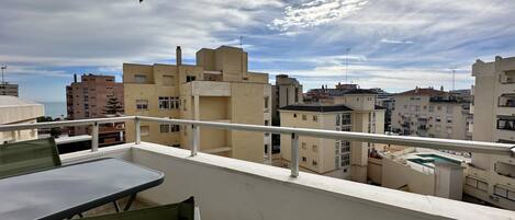 A balcony with a table and chairs, overlooking a cityscape with various buildings.