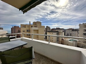 Un balcon avec une table et des chaises, donnant sur un paysage urbain composé de différents bâtiments.