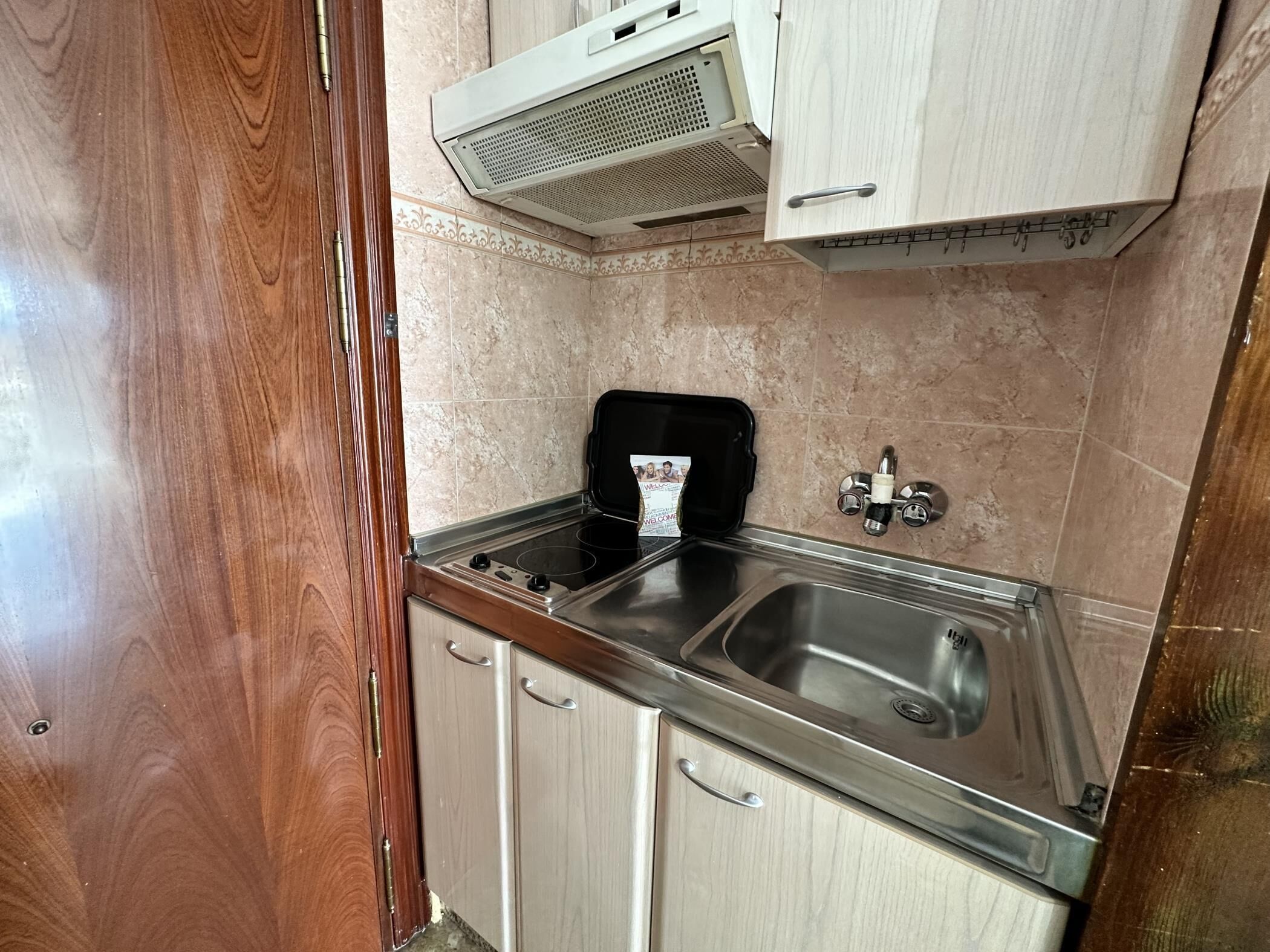 A compact kitchen with a stainless steel sink, a black stove, and wooden cabinets.