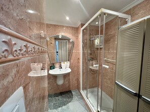 Une salle de bain dotée d’une douche à parois de verre, d’un lavabo sur colonne et d’un miroir de coiffeuse.