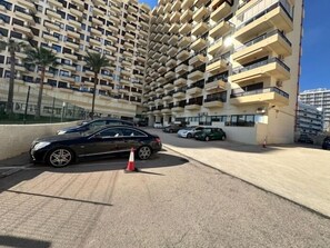 Een meerlaags woongebouw met balkons, een parkeerplaats met auto's en een heldere lucht.