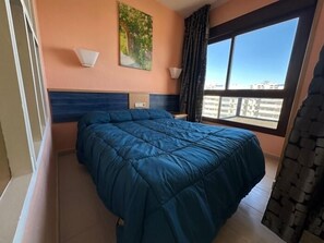 Een slaapkamer met een bed, een raam met uitzicht, een wandlamp en een schilderij.