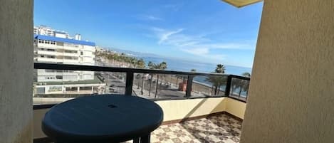 A balcony with a round table, a view of the sea, and buildings in the background.