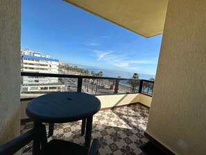 Een balkon met een ronde tafel, uitzicht op zee en gebouwen op de achtergrond.