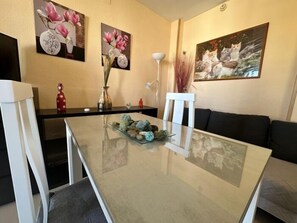 Ein Essbereich mit einem Glastisch, weißen Stühlen und einem schwarzen Sofa.