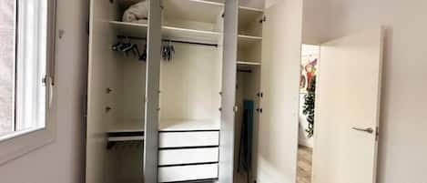 A bedroom with a bed, a closet with open doors, and a door leading to another room.