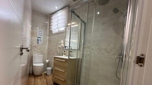 Casa de banho moderna com cabine de chuveiro em vidro, sanita e toucador com espelho.