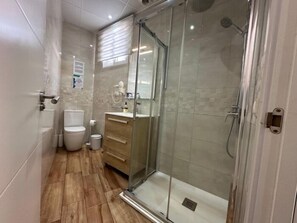 Un bany modern amb un plat de dutxa de vidre, un vàter i un lavabo amb mirall.