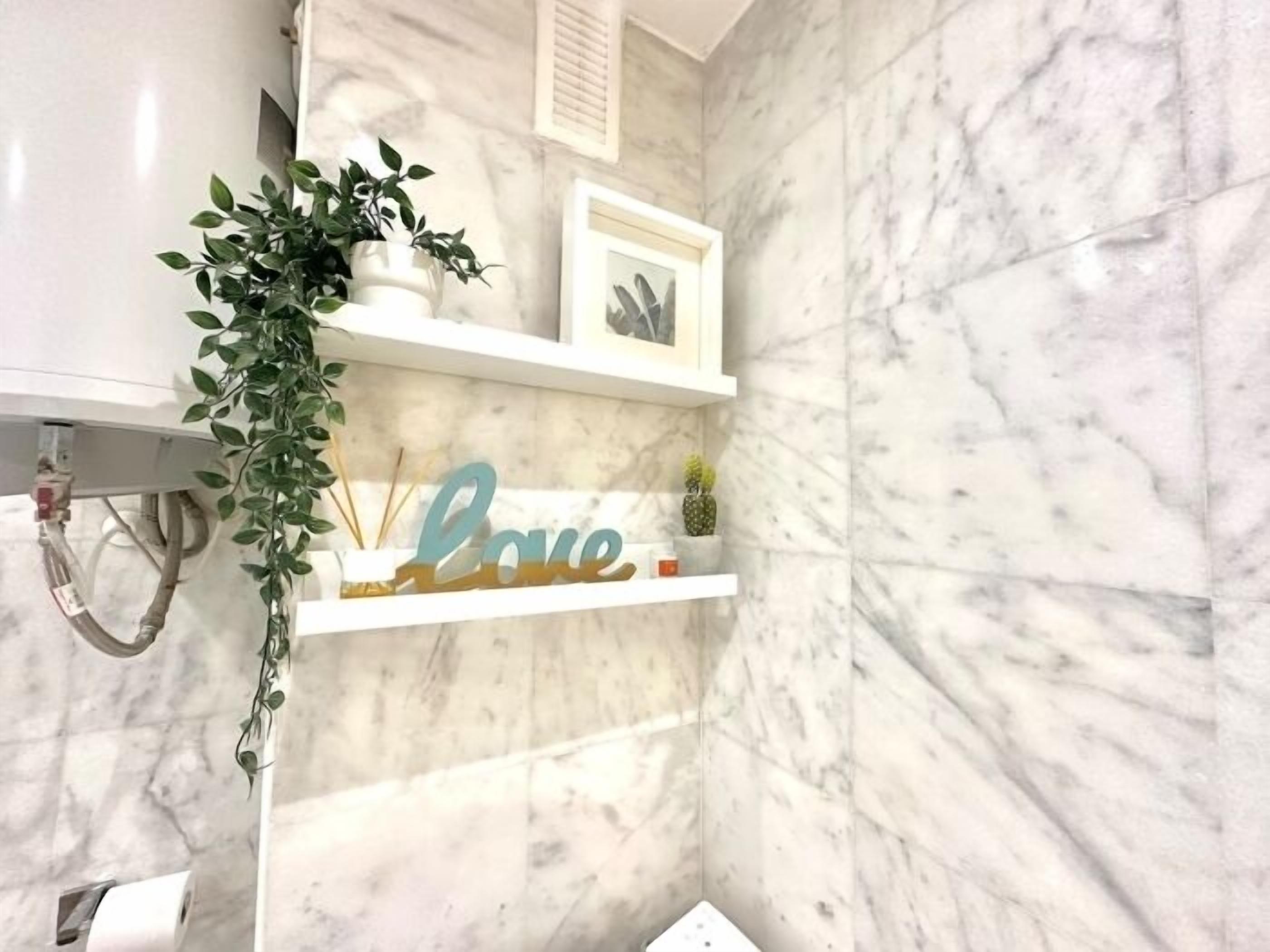 A bathroom with marble walls, a white shelf with a 'Love' sign, and a hanging plant.