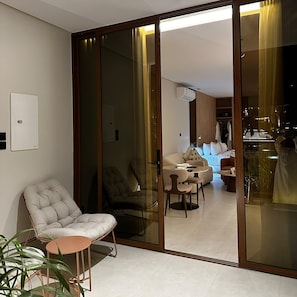Un interior moderno con un divisor de vidrio corredero que da a una sala de estar, una disposición de asientos y un equipo de aire acondicionado visible.