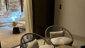 Ein modernes Zimmer mit zwei Korbstühlen, einem kleinen runden Tisch und einem Bett mit weißem Kopfteil.