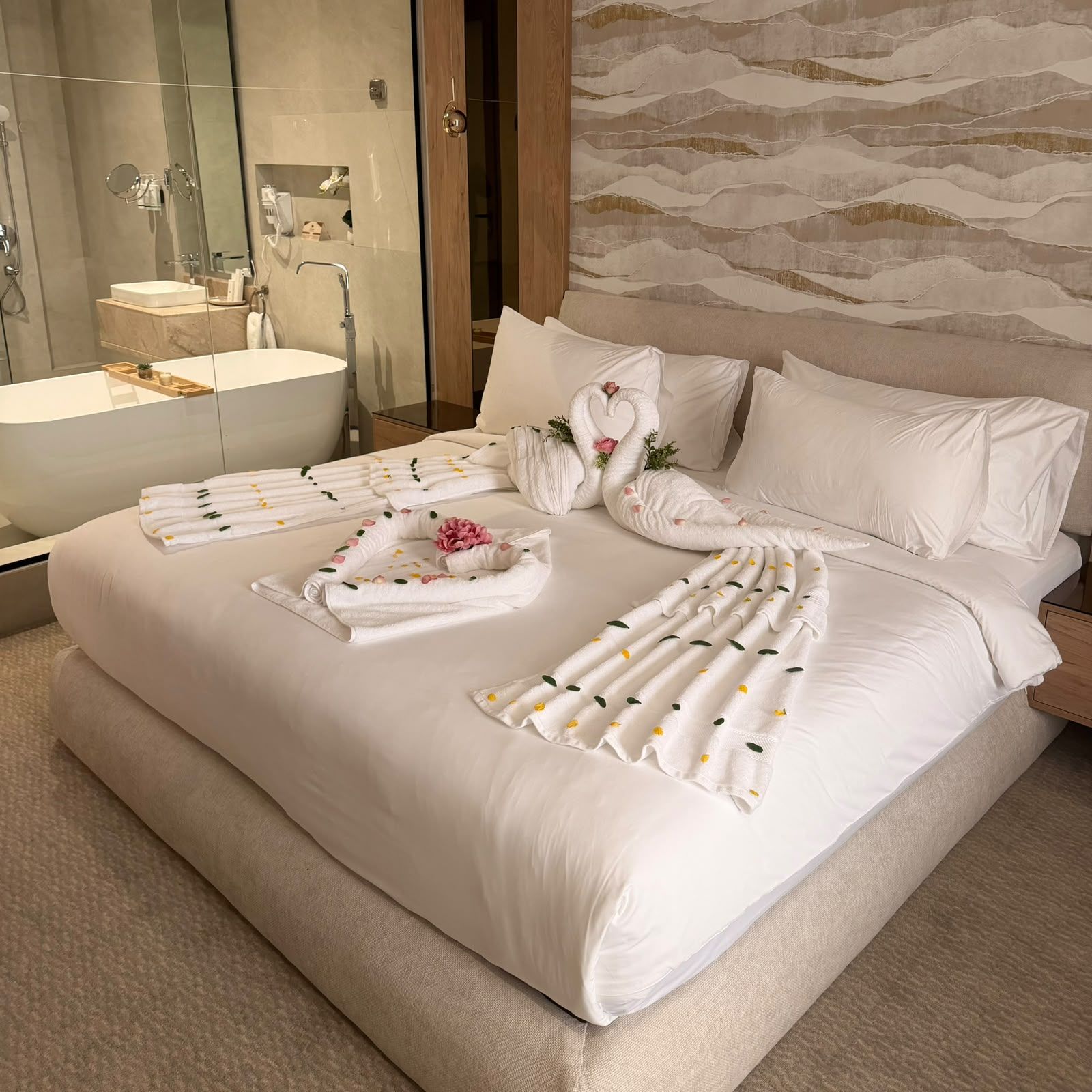 Habitación de hotel con una cama grande, baño con bañera y pared con diseño de olas.