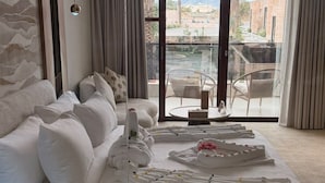 Ein Hotelzimmer mit einem großen Bett, einer Couch und einem Balkon mit Blick auf Gebäude und Hügel.