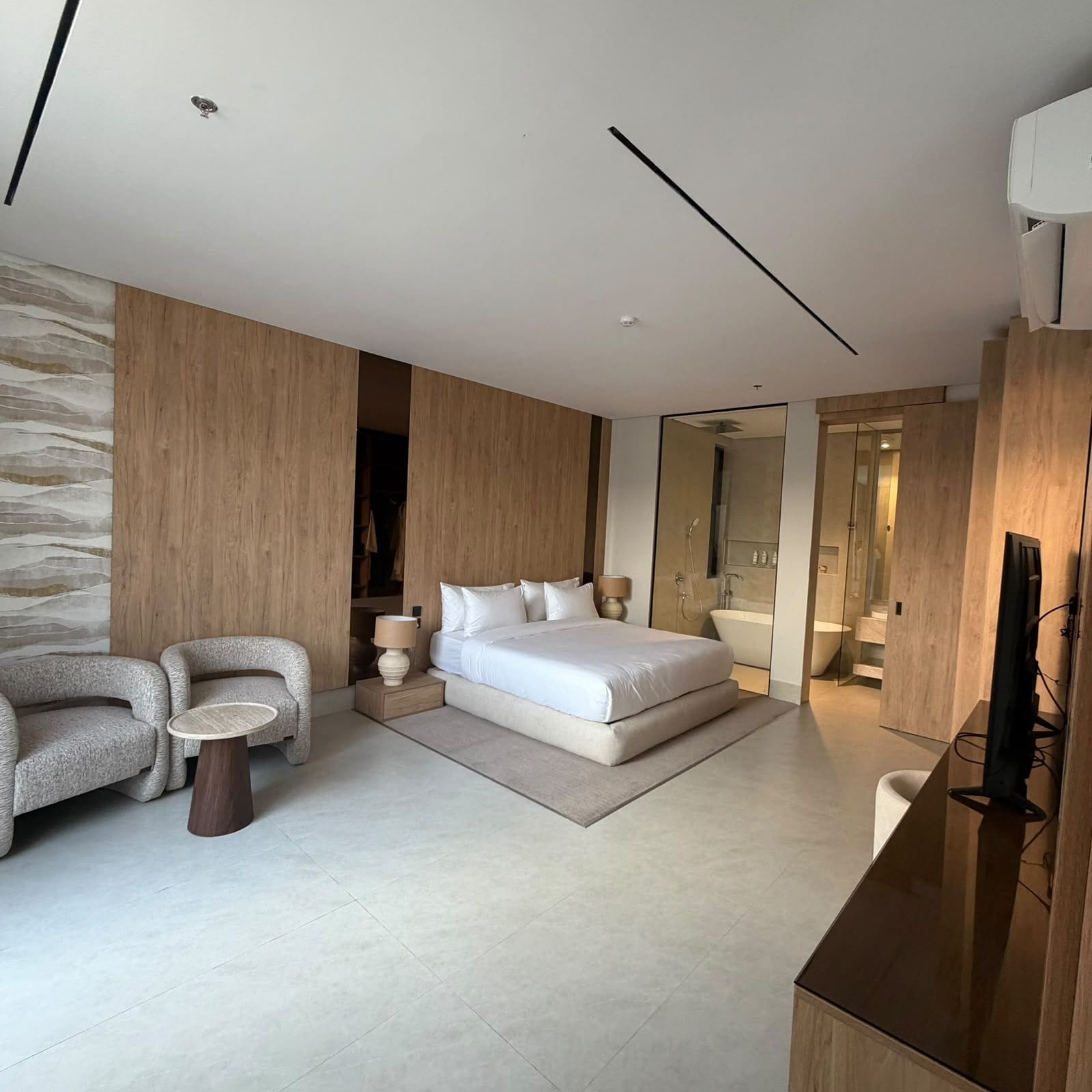 A modern bedroom with a large bed, a seating area with two chairs, a small table, and a television.