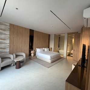 Un dormitorio moderno con una cama grande, una zona de estar con dos sillones, una mesita y un televisor.
