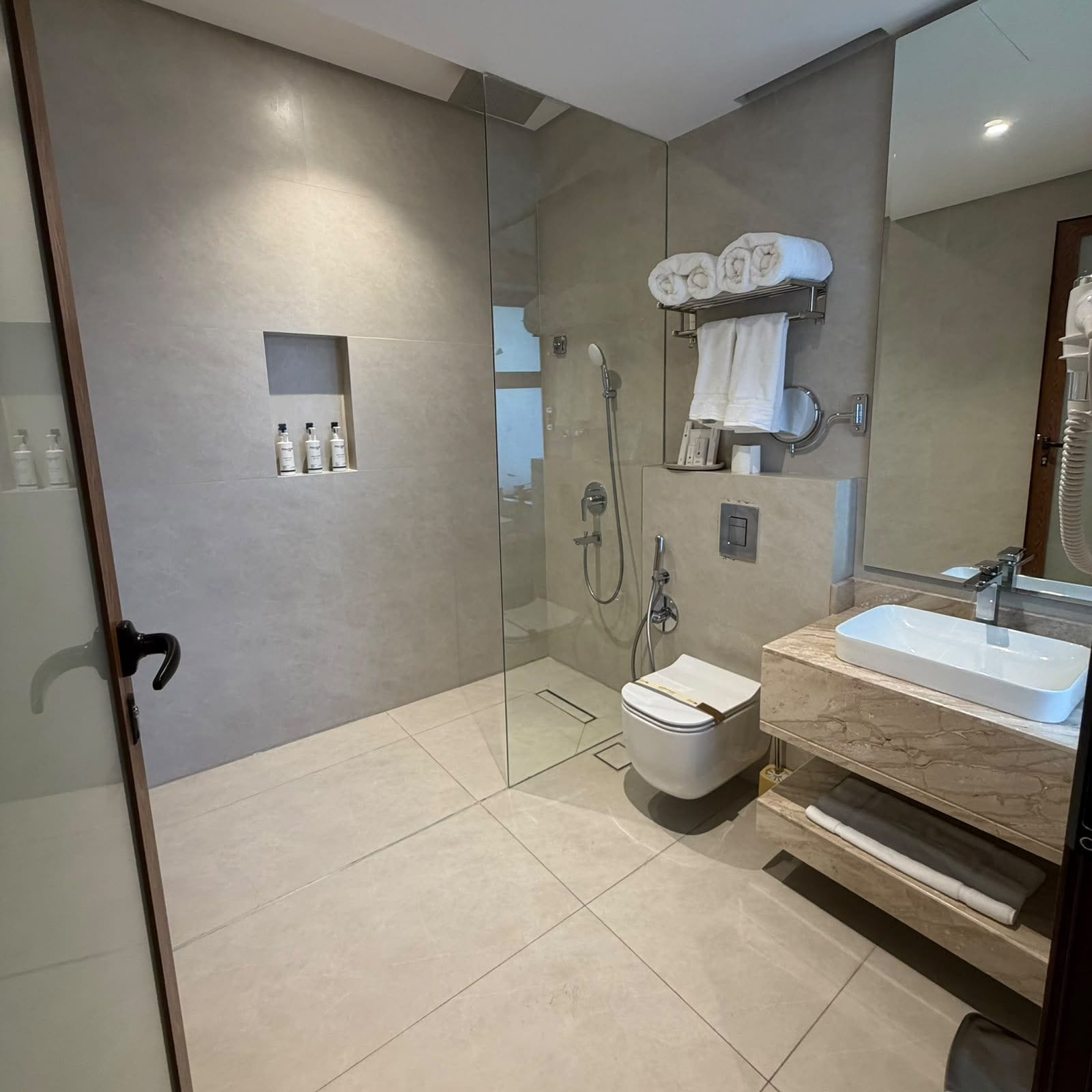 Un baño moderno con ducha envuelta en vidrio, inodoro, lavamanos y perchero para toallas.
