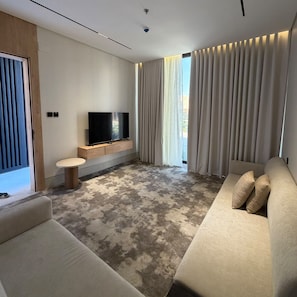 Una sala moderna con un televisor de pantalla plana, un sofá, una mesa de centro y un amplio ventanal con cortinas.