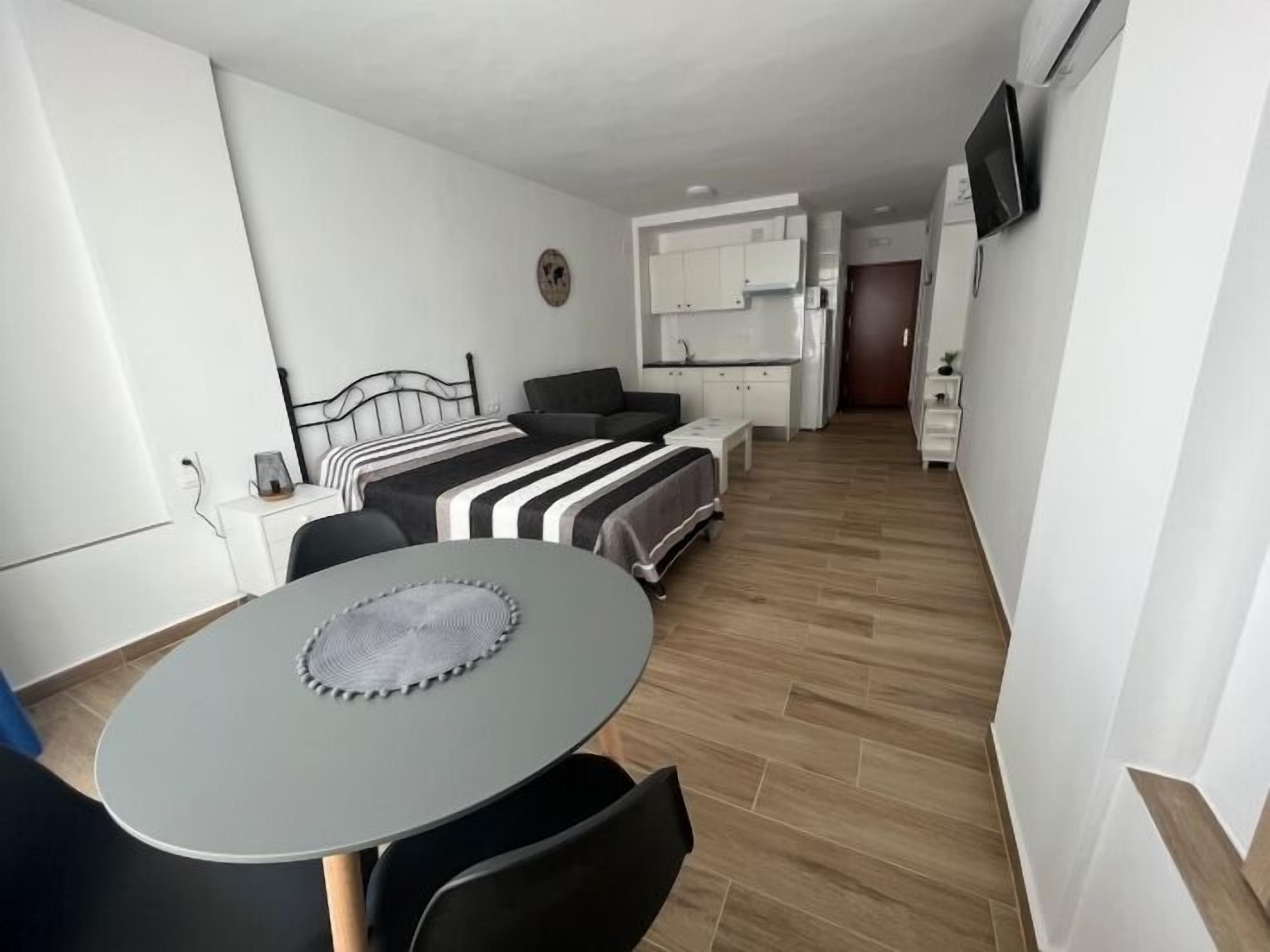Un espace de vie compact comprenant un coin cuisine, un coin repas avec une table et des chaises, et un lit avec une tête de lit.