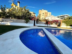 A swimming pool with a curved edge, surrounded by a white wall with a patterned design, and a building with a yellow chimney in the background. - 3-Bedroom Villa with Garden, BBQ and Pool, 350 m from the Beach (Torremolinos)