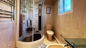 Casa de banho com chuveiro em cabine de vidro, sanita e lavatório.
