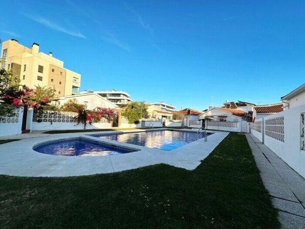 A residential area with a swimming pool, a well-maintained lawn, and a white fence.