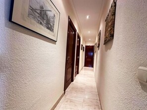 A hallway with a marble floor, wooden doors, and framed pictures on the walls.