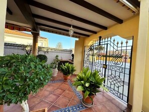A covered patio area with tiled flooring, potted plants, and a decorative metal gate.