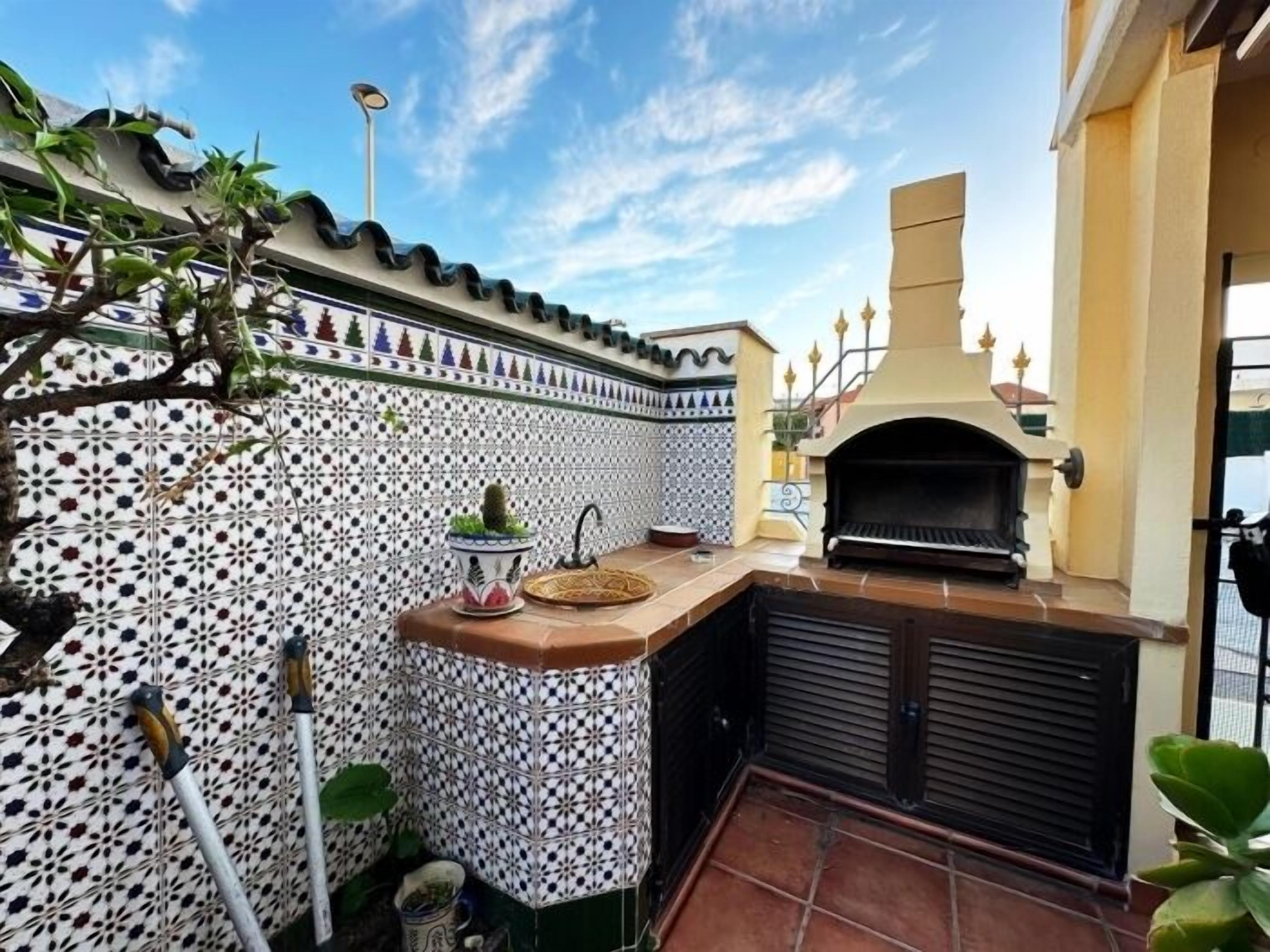 Un patio con un salpicadero de azulejos, una mesita con una planta y un horno de pizza.