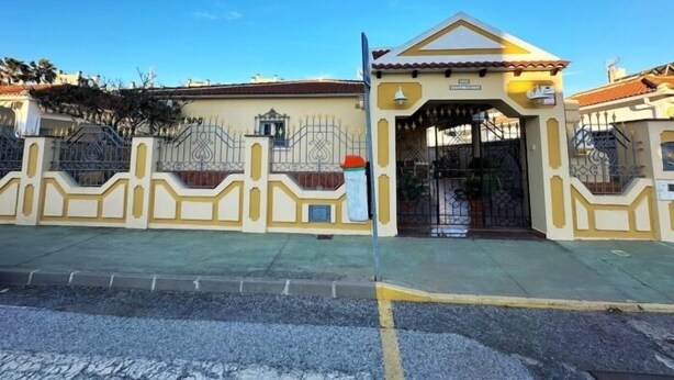 Uma entrada gradeada com portão de metal e pequeno edifício com telhado de azulejos.