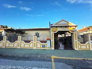A gated entrance with a metal gate and a small building with a tiled roof.