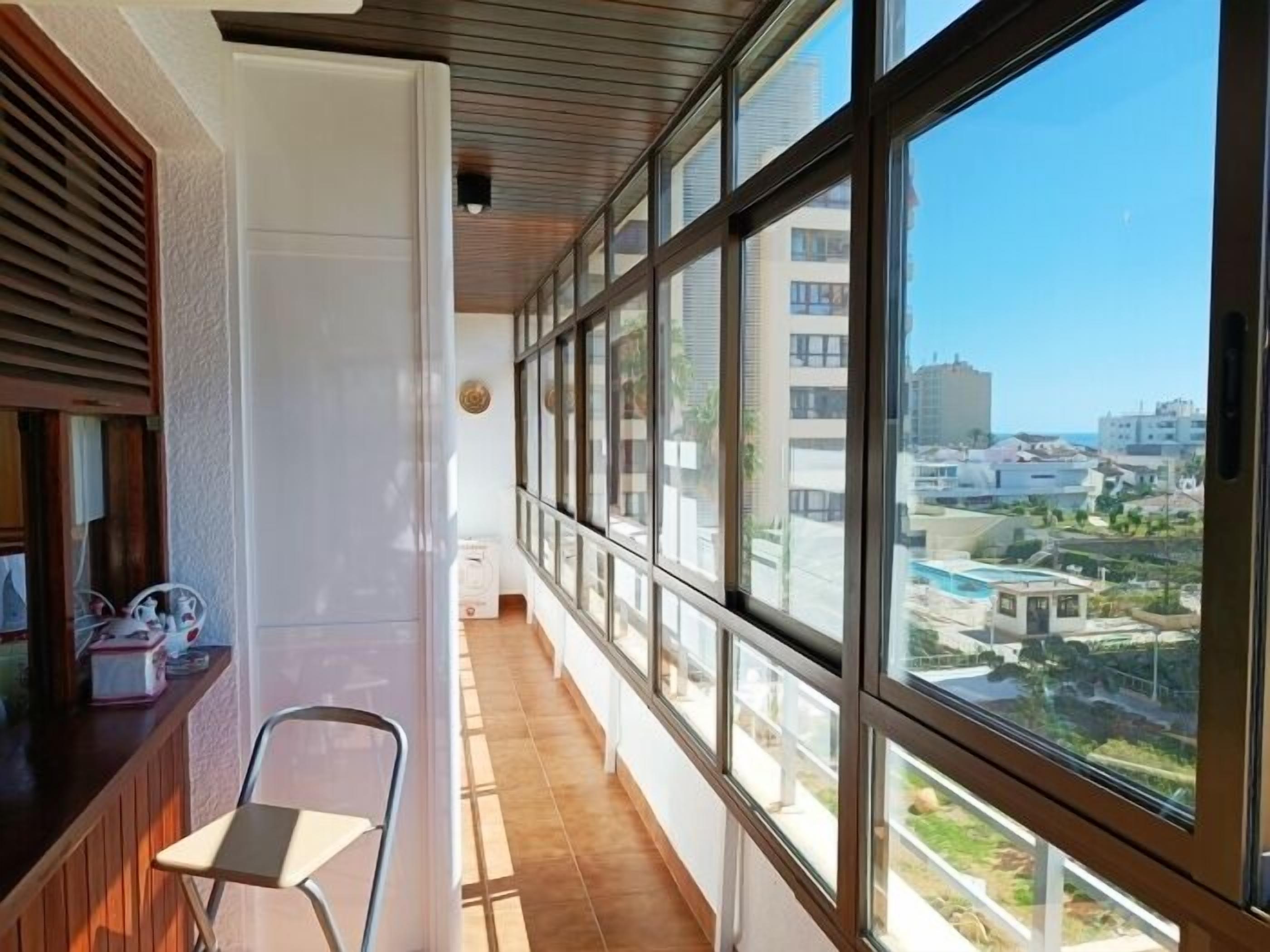 A balcony with a view of a cityscape, a chair, and a window with blinds.