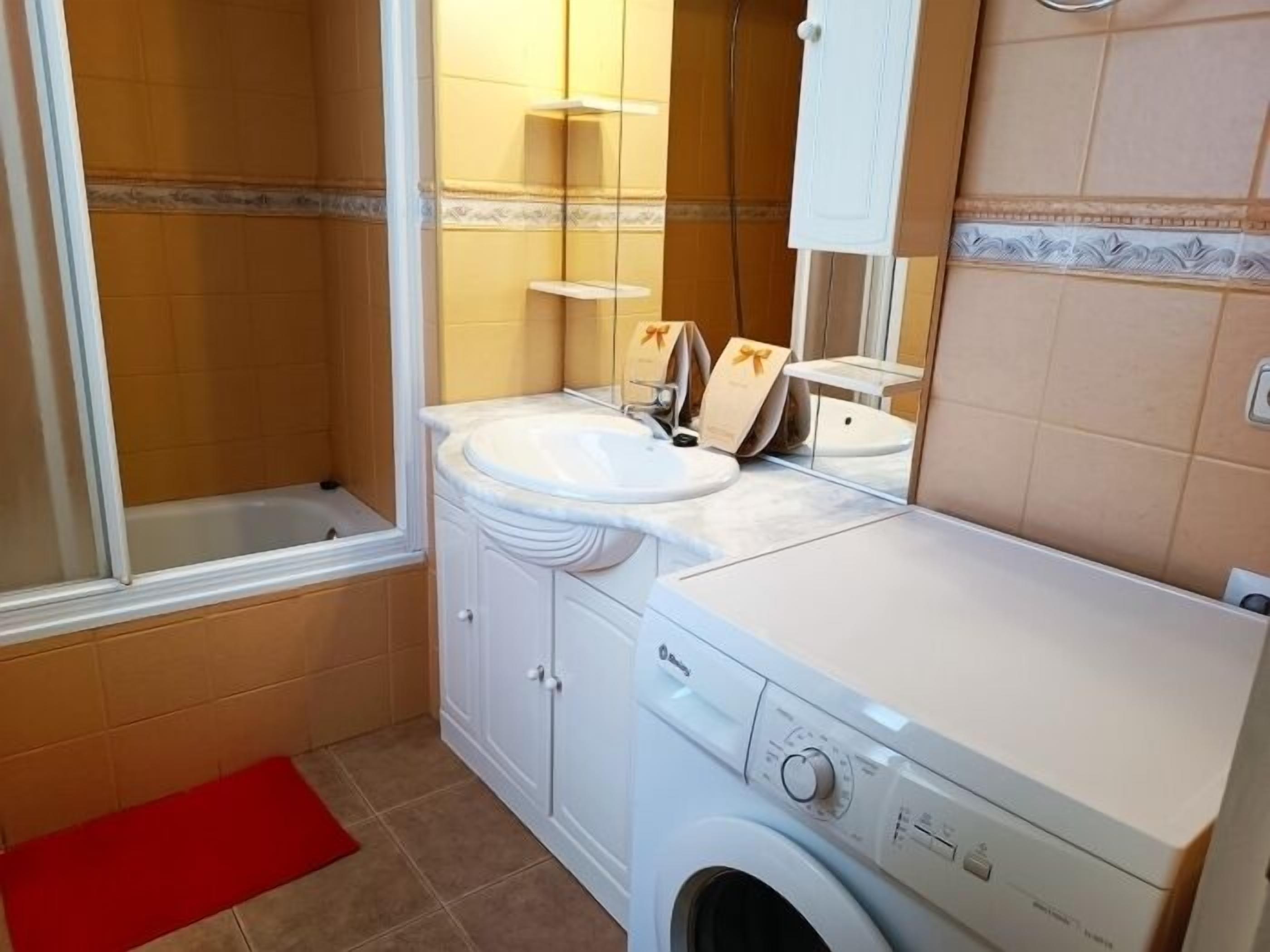 Un baño pequeño con bañera, lavamanos y lavadora.