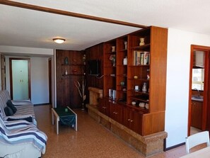 Una sala de estar con una estantería de madera, un sofá, una mesa de centro y una puerta que da a otra habitación.