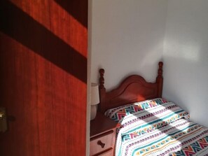 Un dormitorio con cabecera de madera, mesita de noche con lámpara y colcha estampada.