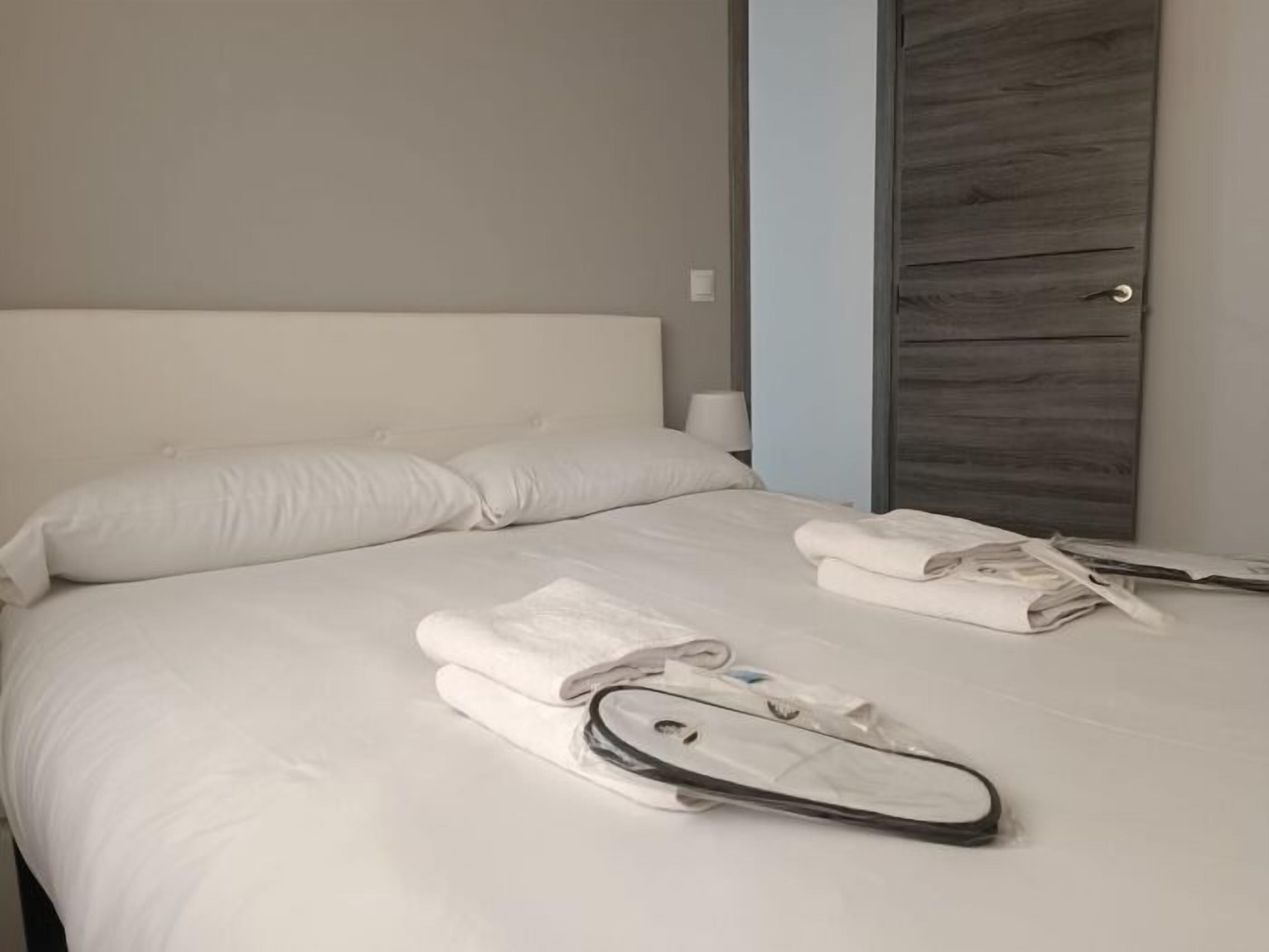 Ein ordentlich bezogenes Bett mit weißen Leinen, zwei gefaltete Handtücher und ein schwarzes Objekt auf dem Bett.