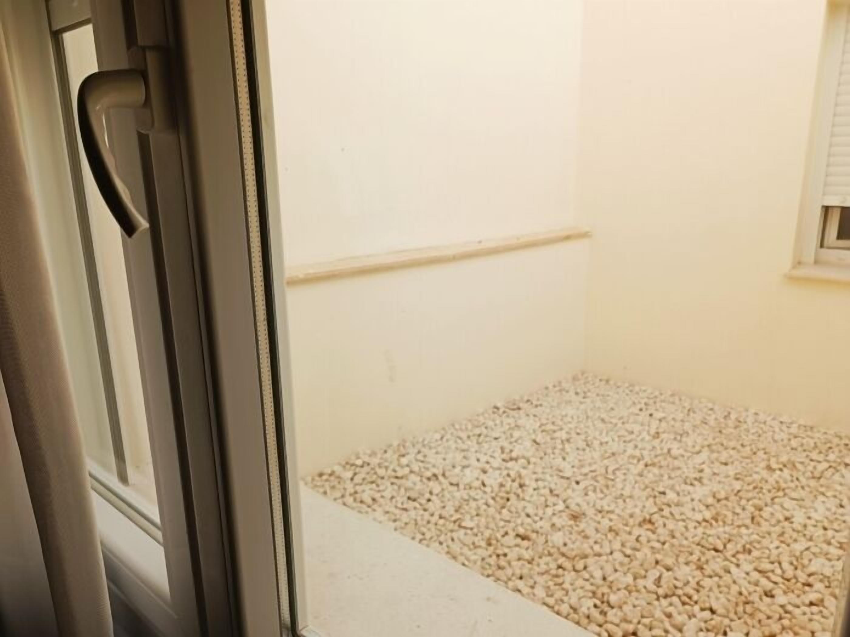 Una habitación con una puerta, una pared blanca y un suelo cubierto de pequeñas piedras.