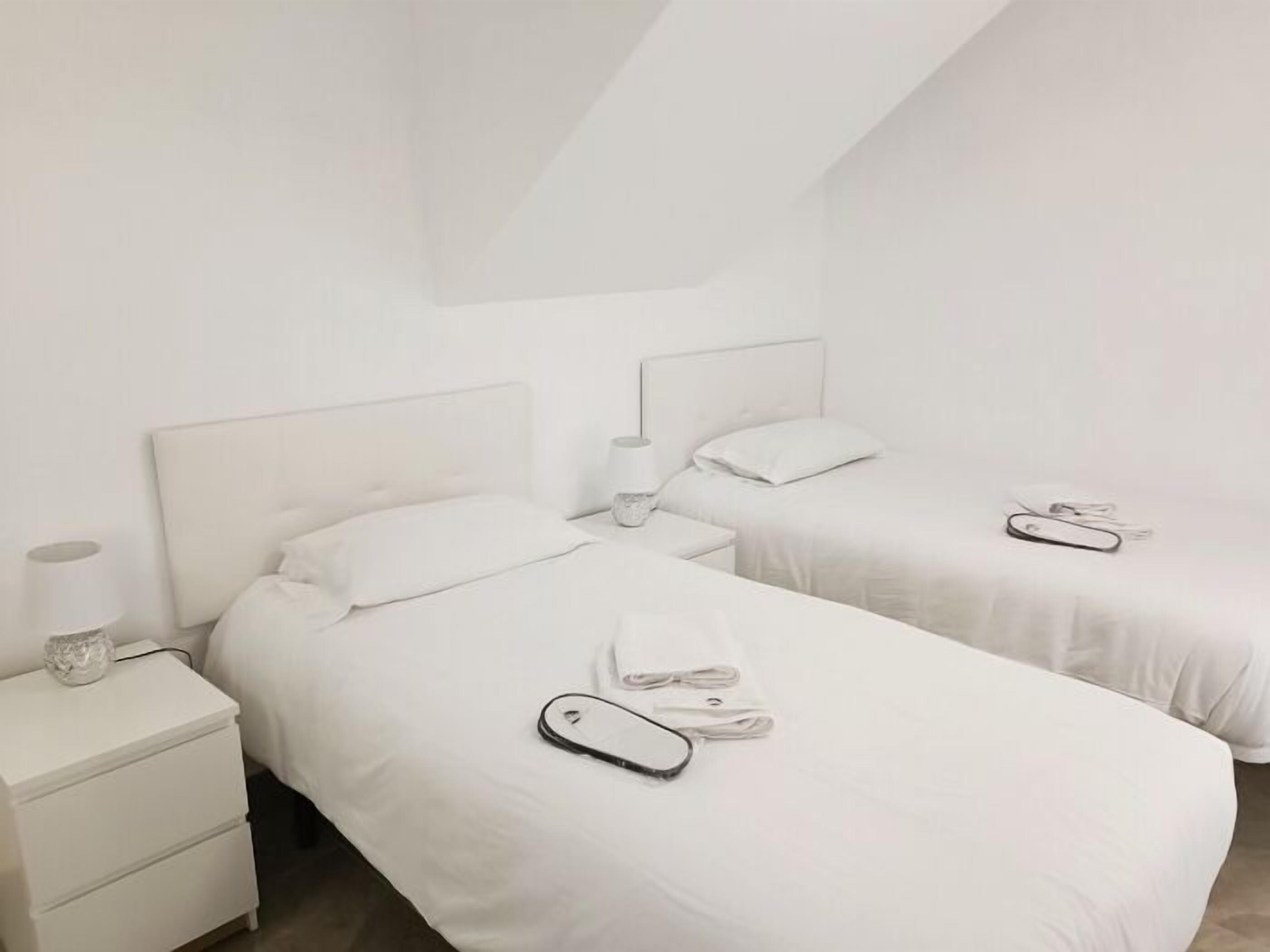 Una habitación de hotel con dos camas, una mesita de noche con lámpara y un tocador con lámpara.
