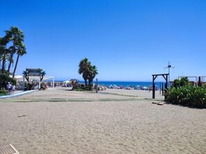 Een strand met een heldere lucht, palmbomen en enkele parasols.