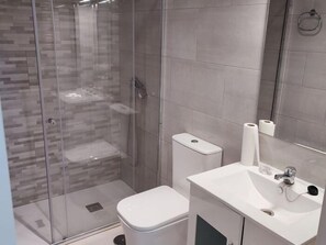 Een moderne badkamer met een douchecabine van glas, een wit toilet en een wastafel met spiegel.