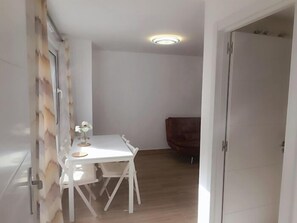 A narrow hallway with a white door, a white table with chairs, and a wooden chair in the background. - Renovated 1-Bedroom Apartment 130 m from the Beach, Bajondillo (Torremolinos)