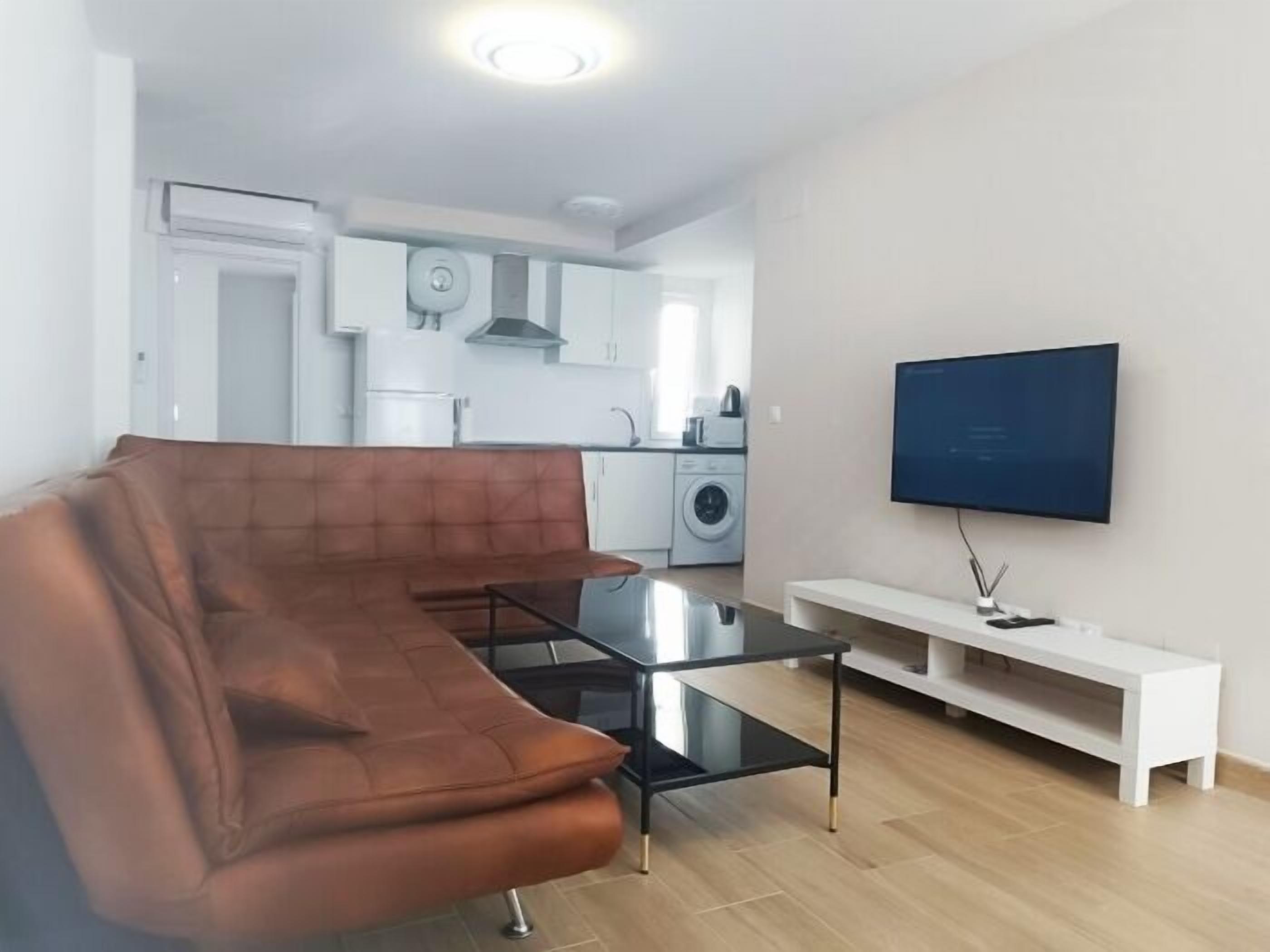 Ein modernes Wohnzimmer mit einem braunen Sofa, einem Glastisch und einem flachbildfernseher an der Wand.