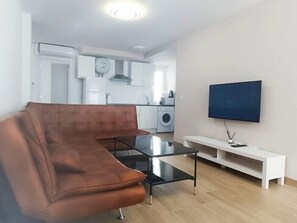 A modern living room with a brown sofa, a glass coffee table, and a flat-screen TV mounted on the wall. - Renovated 1-Bedroom Apartment 130 m from the Beach, Bajondillo (Torremolinos)
